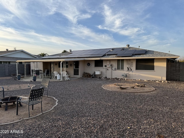 rear view of property with a fire pit, a patio, a fenced backyard, and roof mounted solar panels