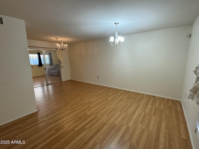 spare room featuring baseboards, a notable chandelier, and light wood finished floors