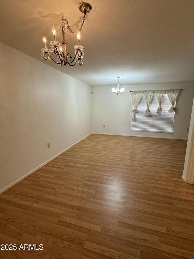 unfurnished room with baseboards, a notable chandelier, and wood finished floors