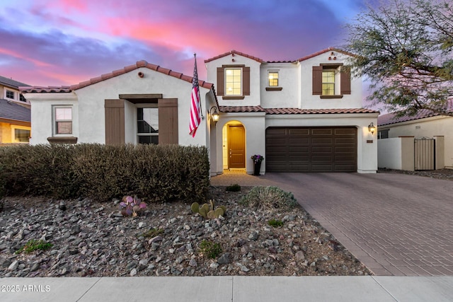 mediterranean / spanish house featuring decorative driveway, a tiled roof, an attached garage, and stucco siding