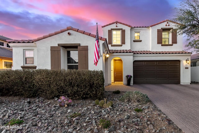 mediterranean / spanish house featuring an attached garage, a tiled roof, decorative driveway, and stucco siding