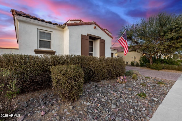 property exterior at dusk featuring a garage, decorative driveway, a tiled roof, and stucco siding