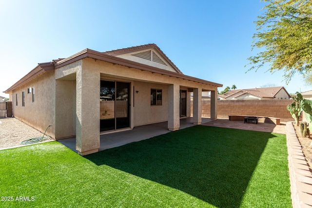 rear view of house with a patio, a fenced backyard, a fire pit, a yard, and stucco siding