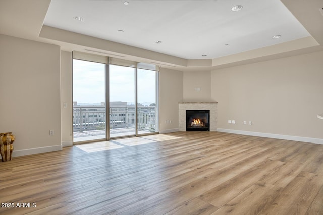 unfurnished living room with a wall of windows, a raised ceiling, light wood-style floors, and baseboards