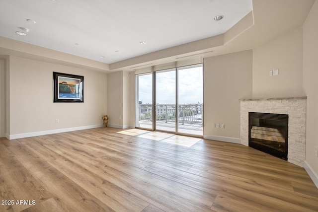 unfurnished living room featuring light wood finished floors, baseboards, a glass covered fireplace, and a wall of windows