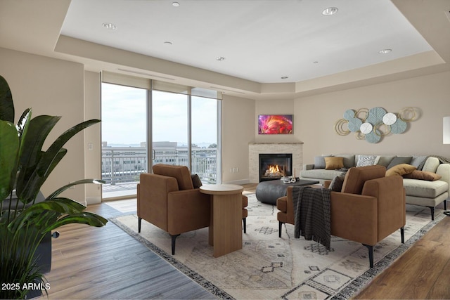 living area with a tray ceiling, light wood-style flooring, a glass covered fireplace, and baseboards