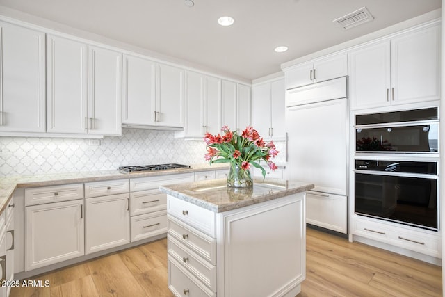 kitchen with visible vents, white cabinets, dobule oven black, stainless steel gas stovetop, and paneled built in fridge
