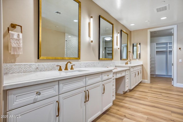 bathroom with double vanity, a walk in closet, visible vents, a sink, and wood finished floors