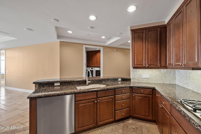 kitchen with a peninsula, separate washer and dryer, a sink, stainless steel appliances, and a raised ceiling