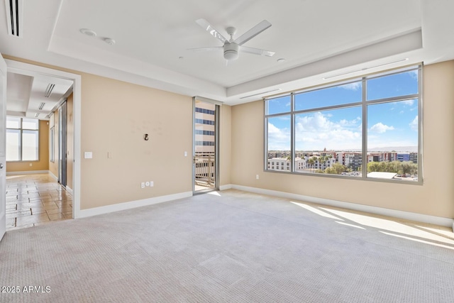 unfurnished room with a raised ceiling, light colored carpet, a ceiling fan, and plenty of natural light
