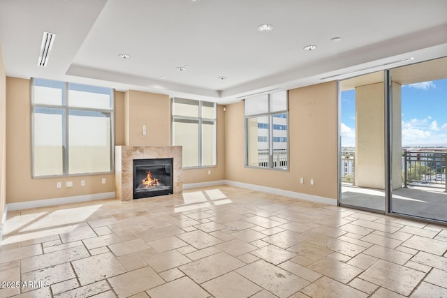 unfurnished living room with a healthy amount of sunlight, a tile fireplace, baseboards, and a raised ceiling