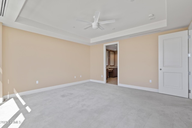 unfurnished bedroom featuring a tray ceiling, light carpet, baseboards, and ensuite bath