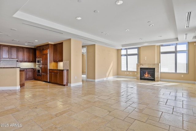unfurnished living room featuring a raised ceiling, stone tile floors, baseboards, and recessed lighting