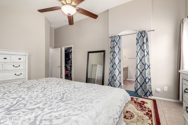 bedroom with a closet, a spacious closet, light tile patterned flooring, ensuite bath, and baseboards