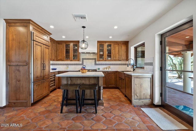 kitchen with paneled refrigerator, backsplash, sink, pendant lighting, and a breakfast bar area