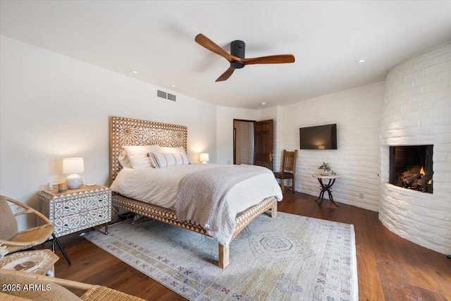 bedroom featuring ceiling fan, a large fireplace, and dark hardwood / wood-style flooring