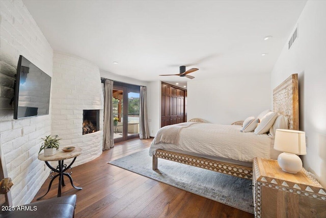 bedroom with access to outside, vaulted ceiling, hardwood / wood-style flooring, ceiling fan, and a fireplace