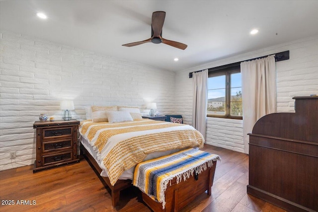 bedroom featuring hardwood / wood-style flooring, ceiling fan, and brick wall