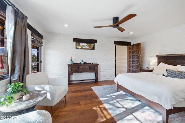 bedroom with ceiling fan, dark hardwood / wood-style floors, and brick wall