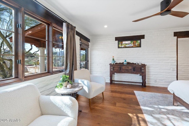 sitting room with ceiling fan, dark hardwood / wood-style flooring, and brick wall