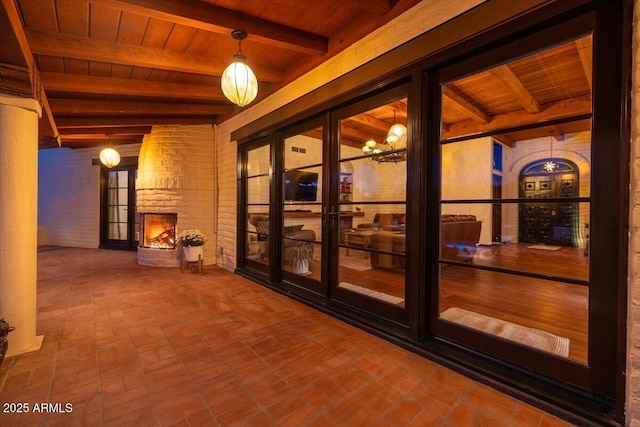 doorway featuring a fireplace, beam ceiling, an inviting chandelier, and wooden ceiling