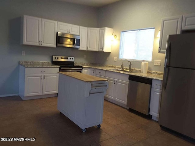 kitchen with appliances with stainless steel finishes, white cabinetry, a kitchen island, and sink