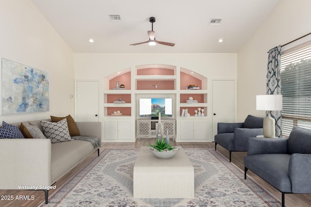 living room featuring built in shelves, ceiling fan, and light wood-type flooring