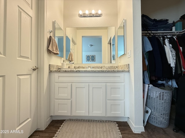 bathroom with a walk in closet, vanity, baseboards, and wood finished floors