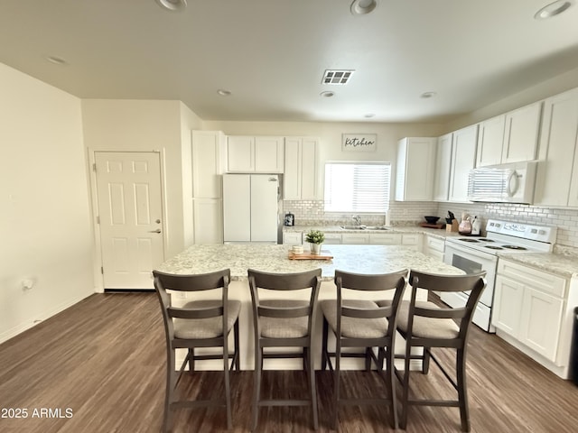 kitchen with white appliances, visible vents, dark wood-style floors, a kitchen breakfast bar, and white cabinetry