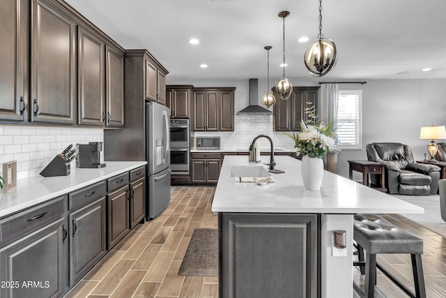 kitchen with a sink, open floor plan, wall chimney range hood, a breakfast bar, and appliances with stainless steel finishes