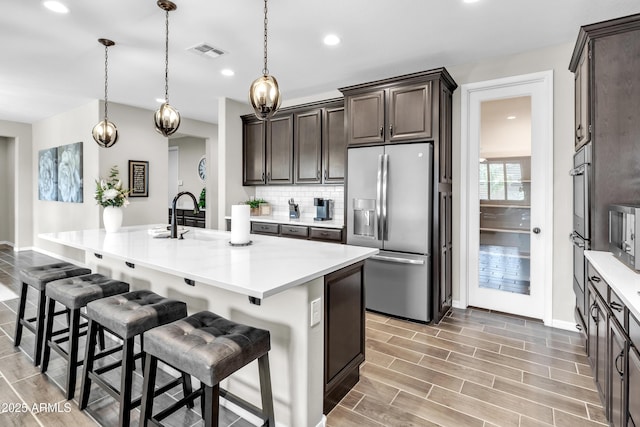 kitchen with a kitchen breakfast bar, dark brown cabinets, decorative backsplash, appliances with stainless steel finishes, and visible vents