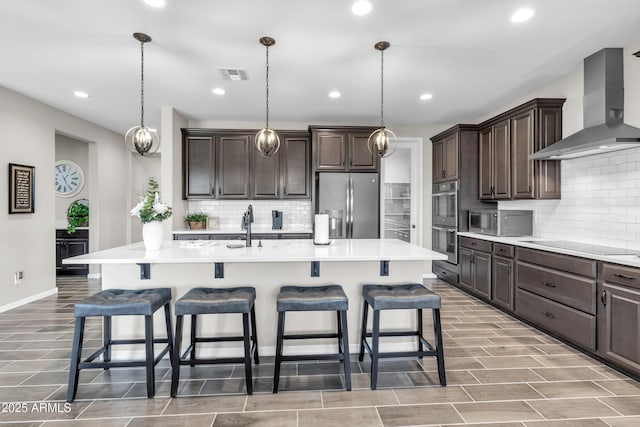 kitchen with wall chimney exhaust hood, stainless steel appliances, visible vents, and dark brown cabinets