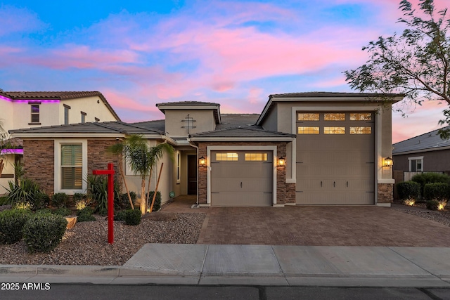 prairie-style house featuring a tile roof, driveway, stone siding, a garage, and stucco siding