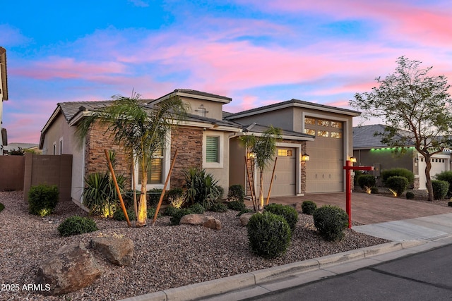 view of front of house featuring driveway, stone siding, fence, a garage, and stucco siding