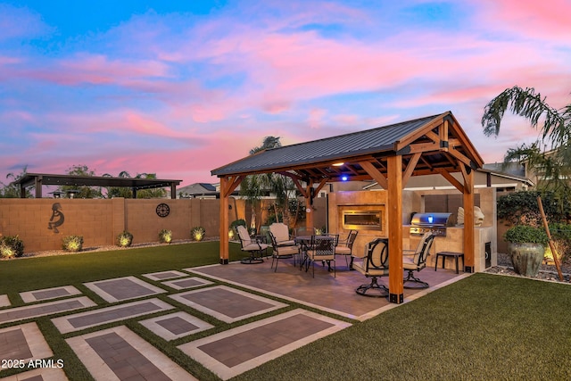 patio terrace at dusk featuring a grill, area for grilling, a fenced backyard, a lawn, and a gazebo
