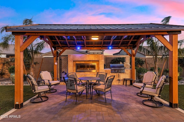 patio terrace at dusk with a gazebo, grilling area, an outdoor kitchen, and outdoor dining area