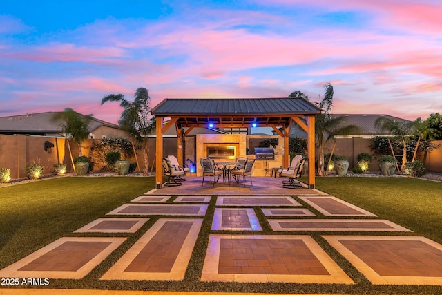 patio terrace at dusk featuring a fenced backyard, a gazebo, a yard, and area for grilling