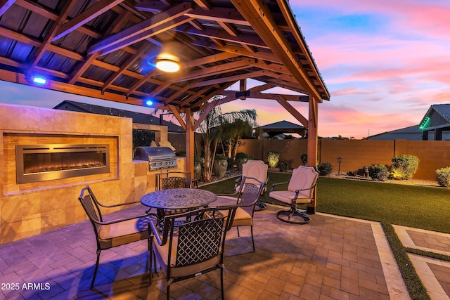 patio terrace at dusk with fence, grilling area, a gazebo, and area for grilling
