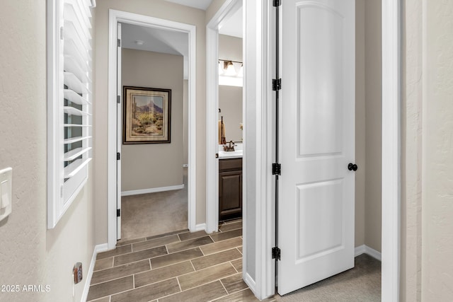 corridor featuring wood finish floors, a sink, and baseboards