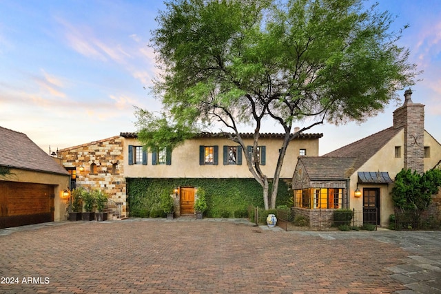 view of front facade featuring stone siding, stucco siding, a chimney, and decorative driveway