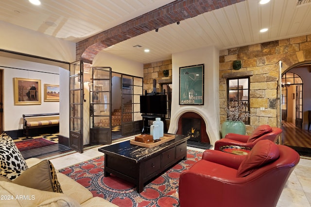 living area featuring arched walkways, beamed ceiling, recessed lighting, and a lit fireplace