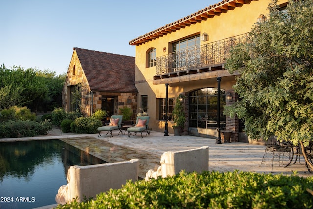 back of house featuring stucco siding, a balcony, stone siding, an outdoor pool, and a patio