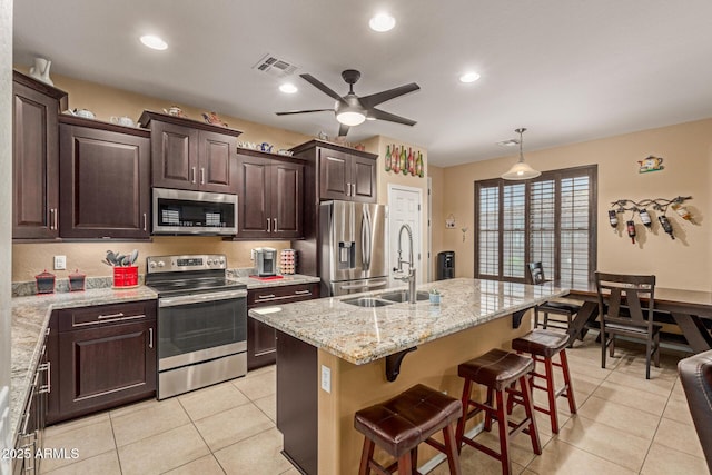 16259 W Papago St, Goodyear, AZ 85338 - kitchen with appliances with stainless steel finishes, light tile patterned floors, ceiling fan, dark brown cabinetry, and a kitchen bar