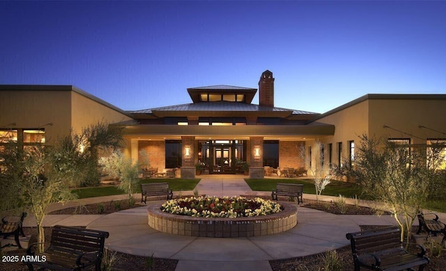 back of property with a standing seam roof, a patio, a chimney, an outdoor fire pit, and metal roof