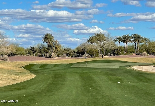 surrounding community with view of golf course, view of wooded area, a putting area, and a lawn