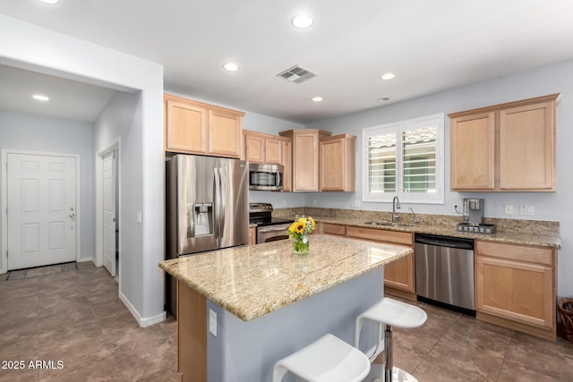kitchen with appliances with stainless steel finishes, light brown cabinets, a sink, a kitchen island, and light stone counters