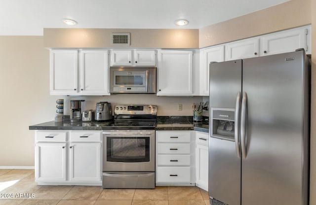 kitchen featuring white cabinetry, stainless steel appliances, light tile patterned floors, and dark stone counters