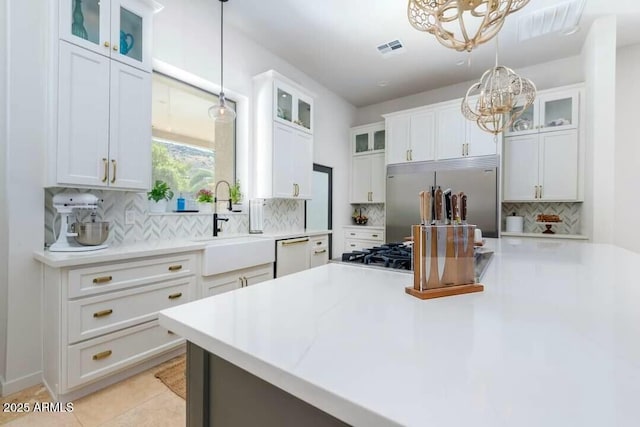 kitchen with built in refrigerator, white cabinets, backsplash, and hanging light fixtures