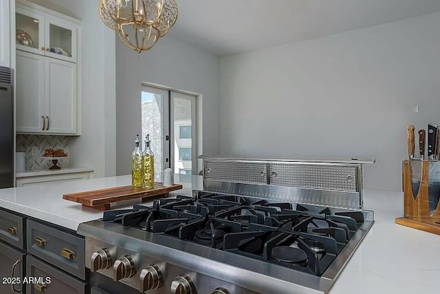 kitchen with a notable chandelier, decorative backsplash, hanging light fixtures, stovetop, and white cabinets