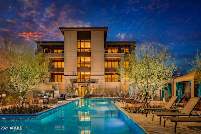 pool at dusk with a fireplace and a patio area